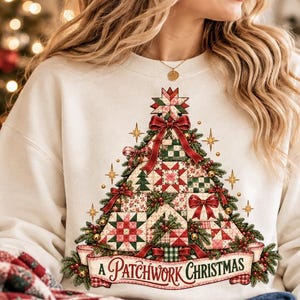 May include: A cream-colored crewneck sweatshirt featuring a graphic of a Christmas tree constructed from various red, green, and white quilt-style patterns. The tree is adorned with red bows and the text A PATCHWORK CHRISTMAS on a banner.