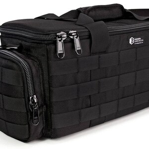 Può includere: Borsa per fotocamera nera con un ampio scomparto con cerniera e una tasca anteriore più piccola. La borsa ha un sistema di cinghie MOLLE e un logo "Hidden Darkness".