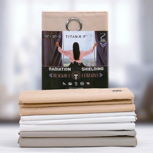 May include: A stack of beige and white blackout curtains with a product label in front. The label reads "TITAN RF™ Radiation Shielding Blackout Curtains" with a graphic of a tower and a sun. The label also states "2 Panels Included" and "84" x "52" inches.