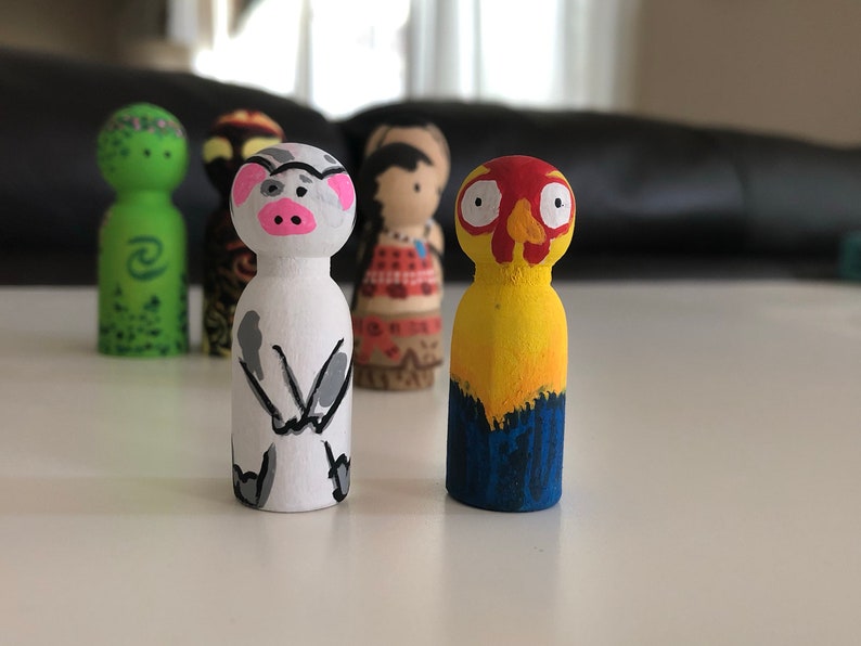 May include: A collection of hand-painted wooden peg dolls. The dolls feature various character designs, including a pig with a pink snout, a yellow and red bird-like figure, and other figures with detailed facial features and clothing.