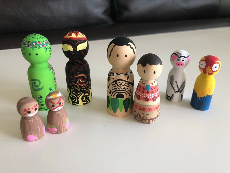 May include: A collection of hand-painted wooden peg dolls. The dolls feature various designs, including floral patterns, tribal motifs, and animal-inspired characters. The color palette includes green, brown, red, yellow, and blue.