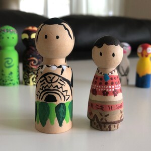 May include: Wooden peg dolls, hand-painted with Polynesian-inspired designs. The dolls feature detailed artwork, including tribal patterns, floral motifs, and vibrant colors. The collection includes dolls with black hair and painted faces.