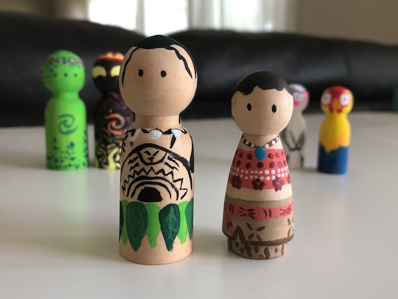 May include: Wooden peg dolls, hand-painted with Polynesian-inspired designs. The dolls feature detailed artwork, including tribal patterns, floral motifs, and vibrant colors. The collection includes dolls with black hair and painted faces.