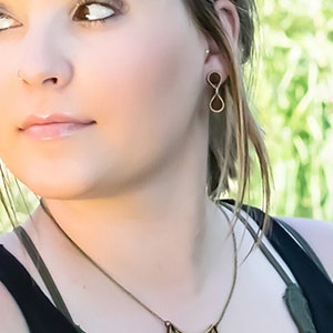 May include: A woman wearing a black tank top with a wooden necklace featuring a crescent moon design. She is also wearing a pair of infinity symbol earrings.