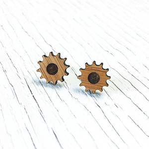Op de afbeelding: Een paar houten oorbellen in de vorm van tandwielen. De oorbellen zijn lichtbruin van kleur en hebben een donkerbruin midden.