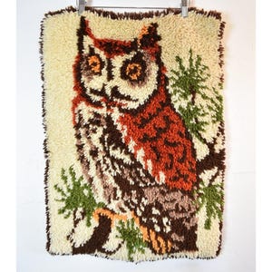 May include: A vintage owl wall hanging. The owl is depicted in shades of brown, orange, and cream, with green accents. The artwork is made of textured yarn, giving it a unique, handcrafted appearance. The owl is perched on a branch.