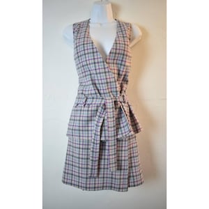 May include: A sleeveless plaid dress in shades of gray, pink, purple, and blue. The dress features a wrap-style bodice with a V-neck and a matching fabric belt. The skirt has a layered design.