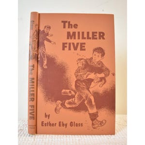 May include: A vintage book titled "The Miller Five" by Esther Eby Glass. The cover is orange with illustrations of a boy running with a dog and another boy. The book's spine also features the title.