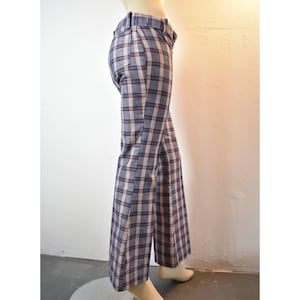 May include: Gray plaid pants with a wide leg design. The pants feature a classic plaid pattern in gray, red, and white. The pants have a high waist and a belt loop detail. The pants are made of a lightweight fabric.