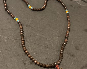 May include: A brown wooden beaded necklace with a silver charm and orange and blue accent beads.