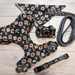 May include: A pet accessory set featuring a dark blue harness, collar, lead, bandana, and waste bag holder, all decorated with a floral pattern of pink flowers and green leaves. Each item includes a black circular patch labelled ALW A LITTLE WOOF.