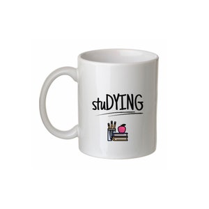 May include: White ceramic coffee mug with the text "studying" in black lettering. A small illustration of a pencil holder, pencils, an apple, and books is below the text.
