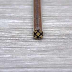 May include: A close-up of a brass pen with a black and gold geometric pattern on the tip.