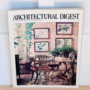 May include: A vintage Architectural Digest magazine cover from January '82. The cover features an interior design scene with framed botanical prints, ornate chairs, and a glass-topped table. The magazine's title is prominently displayed.