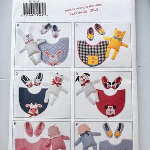 May include: A Butterick 3522 sewing pattern envelope featuring six variations of infant sets, each including a plush toy, a pair of booties, and a bib. Designs include a rabbit, cat, cow, dog, baby, and star-themed set with various colors.