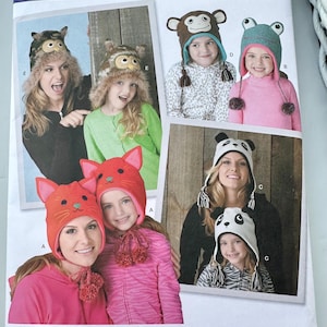 May include: Simplicity sewing pattern 1953 for animal-themed hats. The envelope displays illustrations of hats shaped like an owl, monkey, frog, cat, and panda, each featuring ear flaps and decorative elements like pom-poms or tassels.