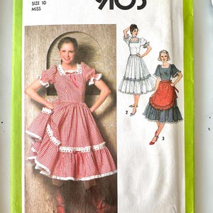 May include: A Simplicity 9103 sewing pattern envelope for a size 10 miss dress. The cover features illustrations of three dress variations with square necklines, puff sleeves, and ruffled hems, including a red and white gingham check design.