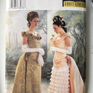 May include: A Butterick sewing pattern envelope 3012 featuring two historical-style gowns. One is a gold brocade dress with off-the-shoulder floral accents, and the other is a peach-colored dress with tiered white lace ruffles and long white gloves.