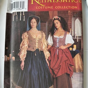 May include: A Simplicity Renaissance Costume Collection sewing pattern envelope featuring two outfits. One includes a gold-sleeved bodice and dark blue skirt with tassel trim. The other features a striped bodice and red skirt over a brown skirt.