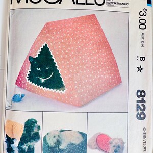 May include: A vintage McCall's sewing pattern envelope. The pattern features a pink cat bed with a black cat silhouette, and images of dog clothing and beds. The envelope has the text "McCall's" and the price $3.00.
