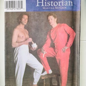 May include: A Simplicity sewing pattern envelope for The Fashion Historian by Martha McCain, number 5033. The cover features two individuals: one wearing white trousers and one wearing a red long-sleeved button-front union suit with a stool.