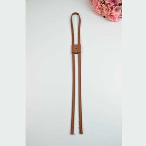 May include: A brown leather strap with a metal button. The strap is about 30 inches long and is perfect for adding a unique touch to a bag or purse.