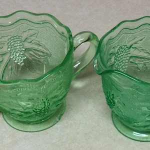 May include: A set of two green glass sugar and creamer bowls with a grapevine design.