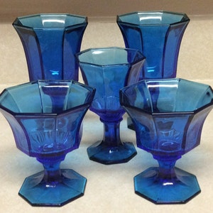 May include: Set of five cobalt blue glass cups with a geometric design. The cups have a wide base and a narrow top.