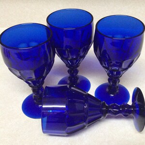 May include: Four cobalt blue glass goblets with a textured design. The goblets are arranged in a group, with one goblet lying on its side.