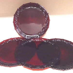 May include: A set of ruby red glass serving dishes. The set includes a large round platter and three oval platters. Each piece has a decorative, scalloped edge.