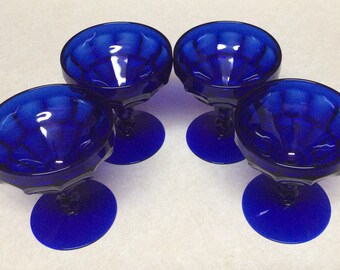 May include: Set of four cobalt blue glass dessert cups with a fluted design. The cups have a short stem and a round base.