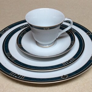 Puede incluir: Juego de té blanco con taza, platillo, plato llano y plato de pan a juego. Los platos y la taza tienen un diseño de borde verde azulado y dorado. El juego es de estilo formal y probablemente para una ocasión especial.