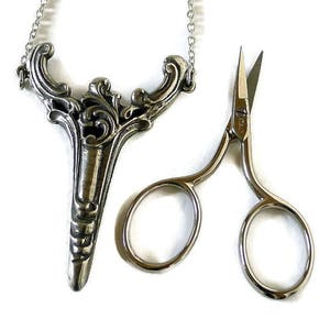 May include: A silver necklace with a decorative pendant shaped like a stylized bird, and a pair of small silver scissors.
