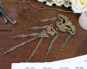 May include: A gold-toned metal chain with a decorative, ornate design. The chain has multiple loops and a large, intricate pendant at the top. The chain is lying on a wooden surface.