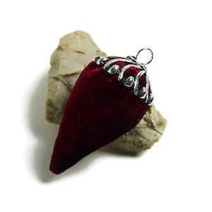 Pode incluir: Um ornamento em forma de lágrima de veludo vermelho com um enfeite de fio de prata e contas.