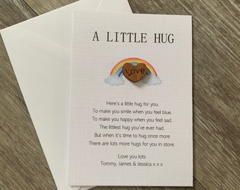 Può includere: Un biglietto con un arcobaleno e un cuore di legno che dice "Love". Il biglietto dice "A Little Hug" e contiene una poesia sugli abbracci. Il biglietto è firmato "Love you lots, Tommy, James & Jessica x x x".