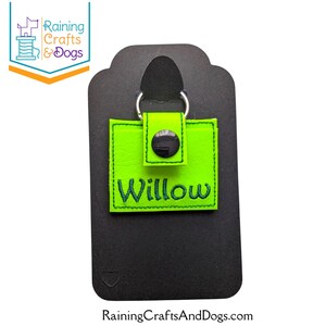 May include: A square, neon green keychain featuring a snap closure and a silver metal ring. The name Willow is embroidered in dark green thread across the front. The keychain is attached to a black display card with a cutout at the top.