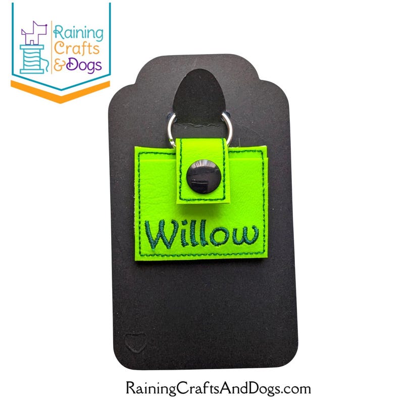 May include: A square, neon green keychain featuring a snap closure and a silver metal ring. The name Willow is embroidered in dark green thread across the front. The keychain is attached to a black display card with a cutout at the top.