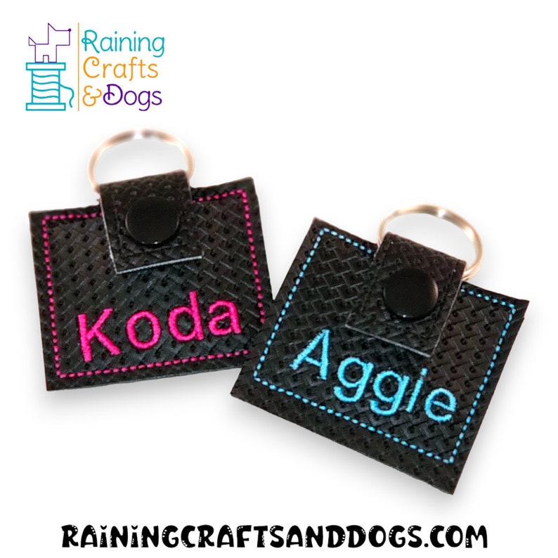 May include: Two square black textured keychains with metal rings and black snap buttons. One keychain features the name Koda embroidered in bright pink thread, while the other displays the name Aggie embroidered in bright blue thread.