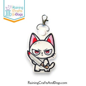 Könnte beinhalten: Weißer Katzen-Schlüsselanhänger mit wütendem Gesichtsausdruck, roten Augen und einem Messer. Die Katze hat rot umrandete Ohren und eine schwarze Umrandung. Der Schlüsselanhänger hat einen silbernen Verschluss und einen weißen Lederriemen. Der Text "Raining CraftsAndDogs.com" steht unten.