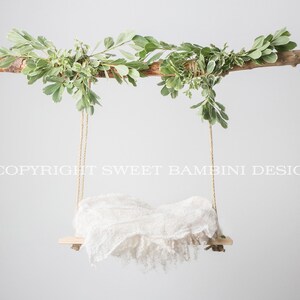 May include: A white fabric swing hanging from a branch with green leaves. The swing is made of a wooden board and rope. The text "COPYRIGHT SWEET BAMBIN DESIGN" is visible in the image.
