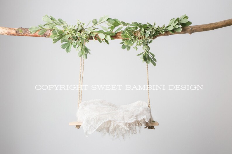 May include: A white fabric swing hanging from a branch with green leaves. The swing is made of a wooden board and rope. The text "COPYRIGHT SWEET BAMBIN DESIGN" is visible in the image.