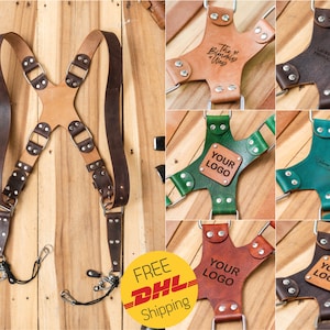Può includere: Un cinturino per fotocamera in pelle marrone con cinturini regolabili e ferramenta metallica. Il cinturino è mostrato con diverse opzioni personalizzabili per il pezzo centrale del cinturino, tra cui un pezzo in pelle marrone con il testo "The Blendedy Way", un pezzo in pelle marrone con il testo "LAKEN SHAPT PHOTOGRAPHY", un pezzo in pelle verde con il testo "YOUR LOGO", un pezzo in pelle blu con il testo "Freedom is Just a Moment Away", un pezzo in pelle marrone con il testo "YOUR LOGO", e un pezzo in pelle nero con il testo "YOUR LOGO".