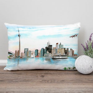 May include: A white pillow with a watercolor illustration of the Toronto skyline, including the CN Tower, and a small airplane flying overhead.