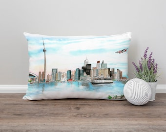 May include: A white pillow with a watercolor illustration of the Toronto skyline, including the CN Tower, and a small airplane flying overhead.