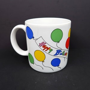 May include: White ceramic mug with a colorful balloon design and the text "Happy Birthday".