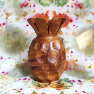 May include: A wooden pineapple shaped bowl with a textured surface and holes throughout. The bowl is brown and has a natural wood finish.