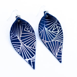 May include: A pair of blue leather earrings with a white geometric pattern. The earrings are teardrop shaped and have silver hooks.