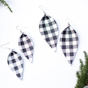 May include: A pair of black and white checked dangle earrings. The earrings are shaped like a teardrop and have a silver hook.