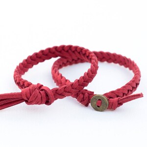 Può includere: Due braccialetti in pelle intrecciata rossa con una chiusura in metallo. Un braccialetto ha un fiocco.